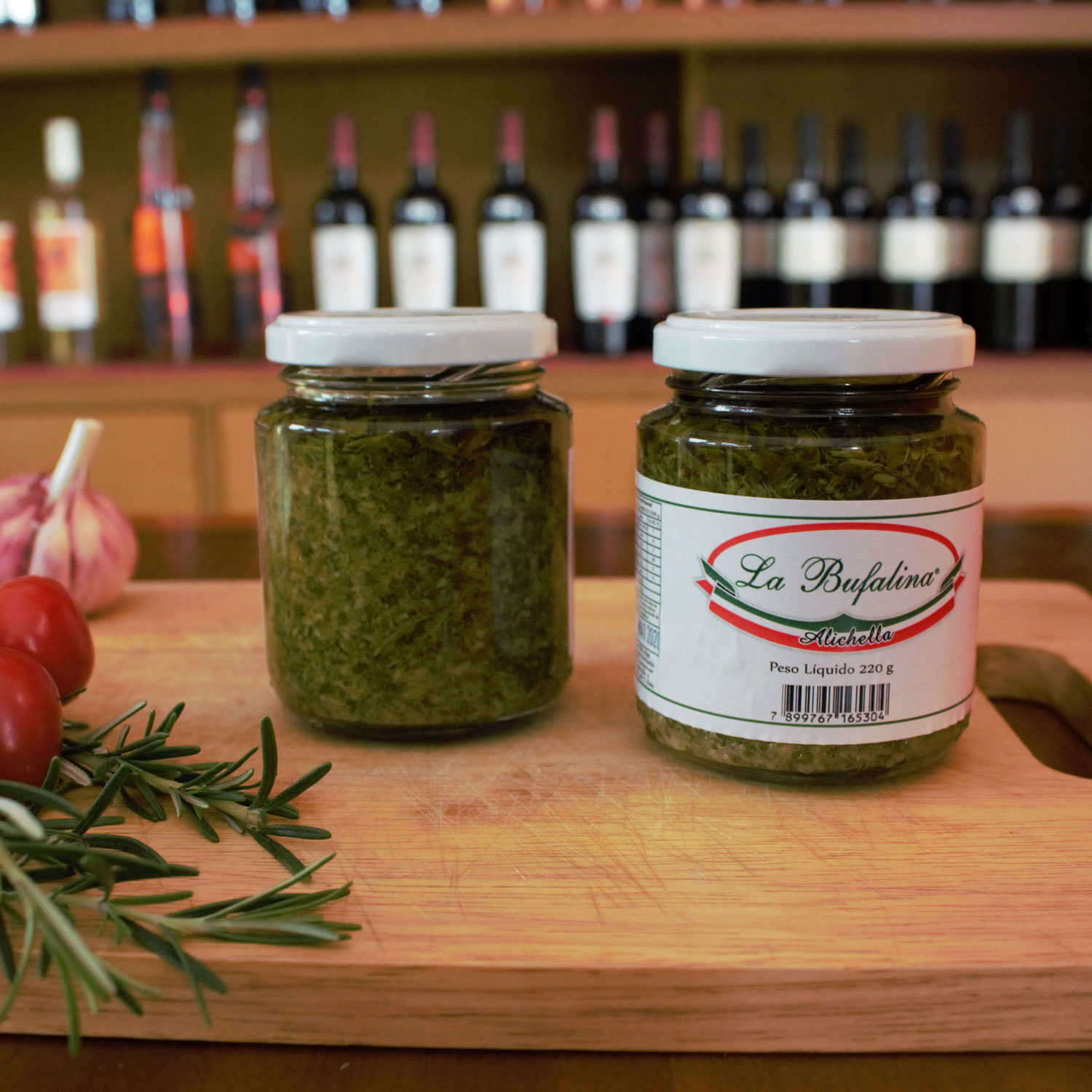 Dois potes de antepasto Alichella sobre tábua, com garrafas de vinho ao fundo