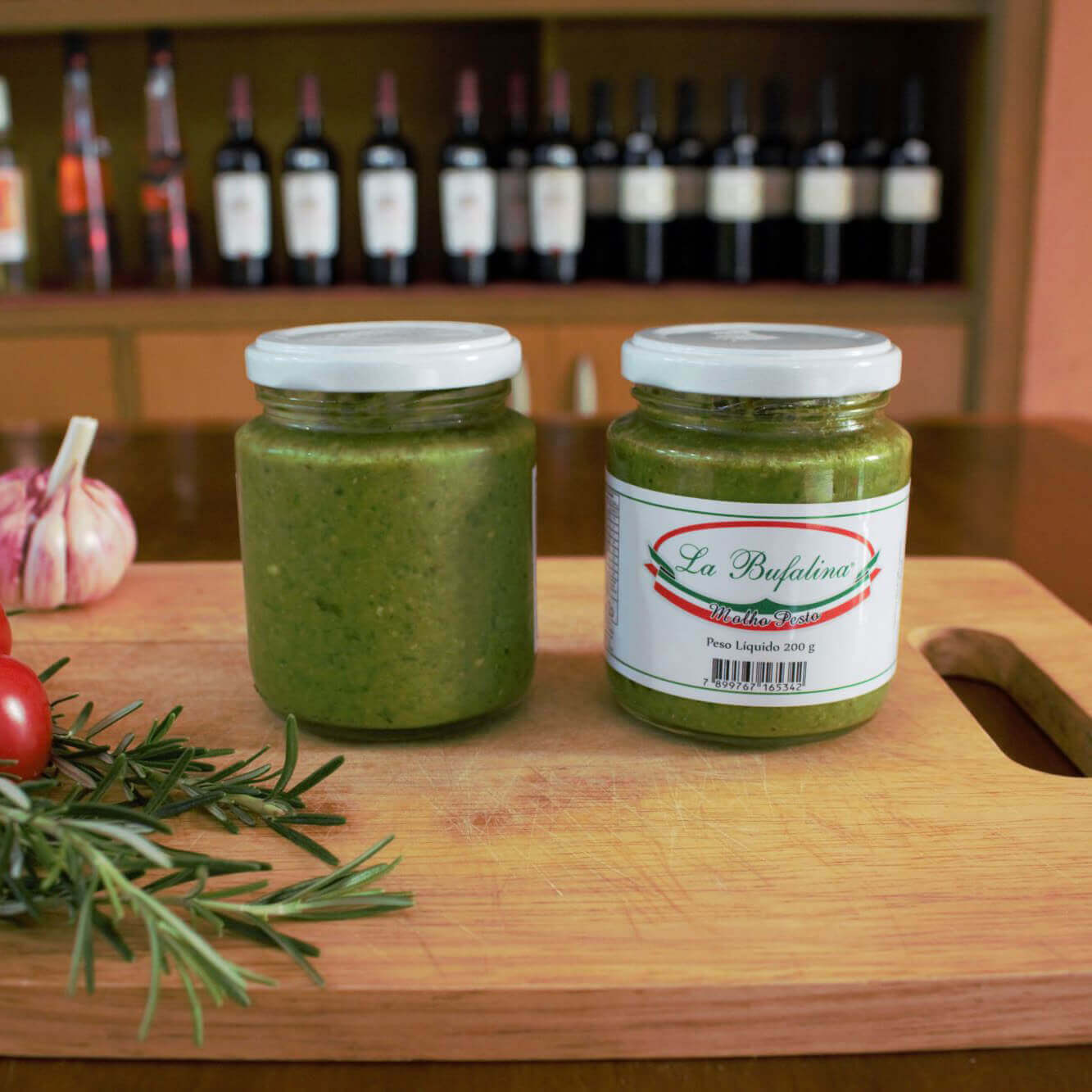 Dois potes de molho pesto sobre tábua, com garrafas de vinho ao fundo